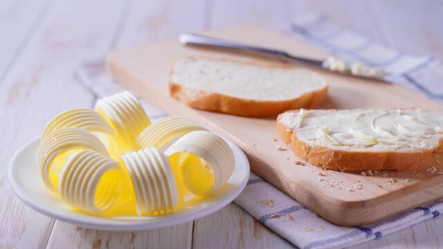 A buttered slice of wheat bread on a cutting board.
Delicious white wheat bread and fresh butter curls on cutting board.
