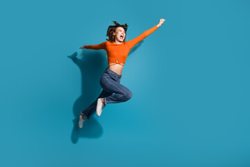 Obraz premium Young woman jumping happily in casual outfit against a vibrant blue background, expressing joy, energy, and freedom