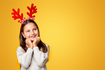 Make a wish. Dreamy child with horns in sweater looks up at empty space, isolated on yellow...