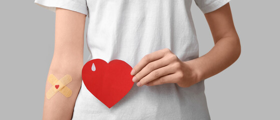 Woman with applied medical patches and paper heart on grey background. World Blood Donor Day
