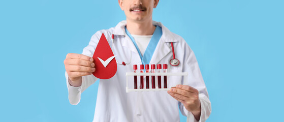 Male doctor with paper blood drop and test tubes on blue background, closeup