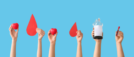 Female hands holding blood pack, test tube, hearts and paper blood drops on blue background. Blood donation concept