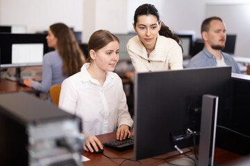 Fototapeta premium Young female teacher helping young female trainee work at computer in office