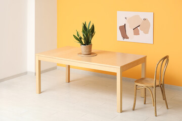 Stylish dining table with houseplant near orange wall in room