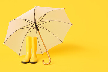 Stylish white umbrella and gumboots on yellow background