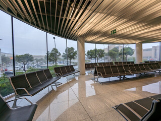 Spacious modern airport waiting longue area with empty rows of chairs seating, large panoramic glass window wall, urban surroundings view, cloudy sky. Contemporary architecture, travel, quiet space. 