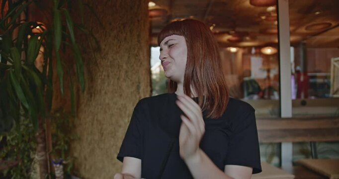 A young woman sits in a cafe, trying a new drink she ordered. She finds it disgusting at first, before her expression turns to one of pleasant surprise.