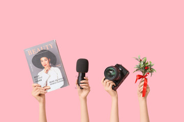 Journalist's female hands with Christmas branch, camera, magazine and microphone on pink background