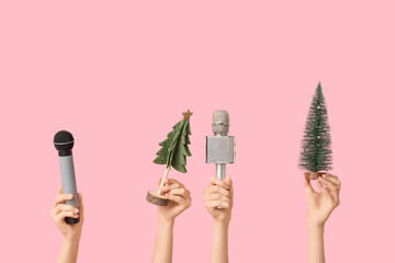 Journalist's female hands with Christmas fir trees and microphones on pink background