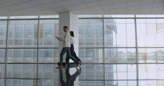 Business partners walk and discuss something in a modern office space. A woman and a man walk through a spacious office area, discussing a business project.