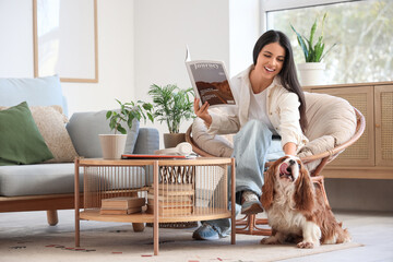 Beautiful young woman with fashion magazine and cute cavalier King Charles spaniel at home