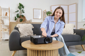 Young woman with modern projector on coffee table in stylish living room
