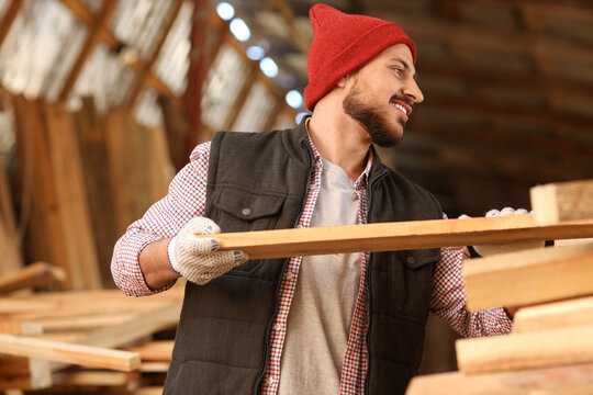 Young carpenter with wooden planks working at sawmill