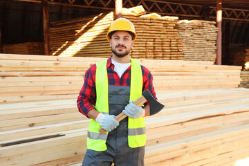 Young carpenter in reflective vest with axe at sawmill