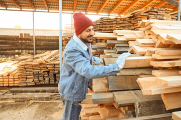 Handsome carpenter near wooden planks at sawmill