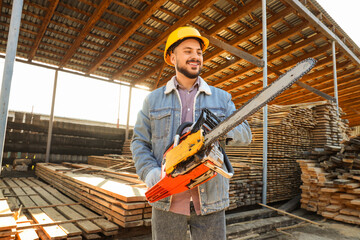 Male carpenter in hardhat with electric saw at sawmill