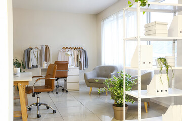 Interior of clothing store office with workplace, houseplants and stylish clothes on racks