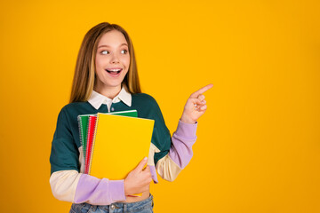 Happy young student holding colorful notebooks pointing in excitement against a vibrant yellow background