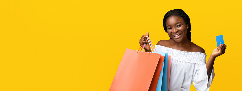 Easy Payments. Smiling Black Young Woman Holding Shopping Bags And Credit Card With Contactless Paypass Payment Option, Enjoying Safe Purchases, Isolated Over Yellow Background, Free Space