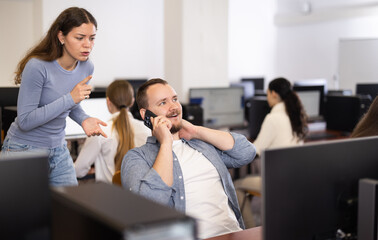 Young woman makes remark to young man talking loudly on mobile phone in office space