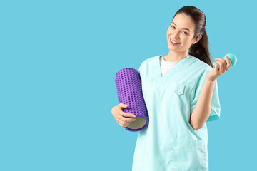 Female physiotherapist with foam roller and massage ball on blue background