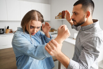 Young man beating his wife in kitchen. Domestic violence concept