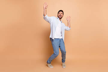 Young bearded man in casual fashion dancing expressively on beige background showing gestures with...