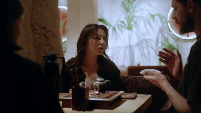 Two guests sit at a wooden table as the tea master talks about the tea's origins and lets them enjoy its scent in an interesting and stylish teahouse setting.