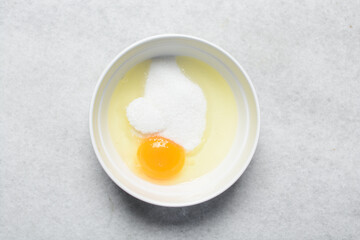 Overhead view of egg and sugar in a bowl on a marble countertop