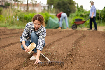 Portrait of positive peasant girl while working in garden and planting seeds of fruit plants....