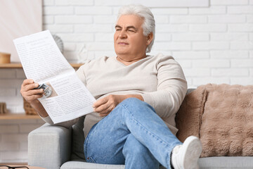 Fototapeta premium Handsome senior man reading newspaper and sitting on sofa in living room