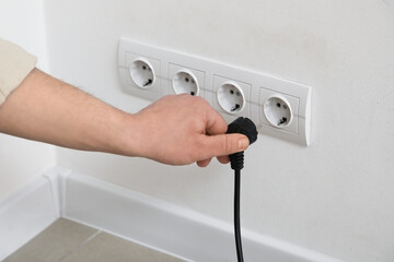Male hand getting out plug from socket on light wall at home, closeup