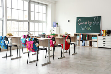 Blackboard with text GOODBYE SCHOOL and drawn boat on light wall in classroom interior