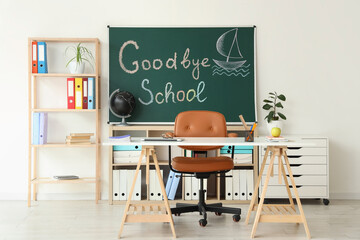 Blackboard with text GOODBYE SCHOOL and teacher's table in classroom interior
