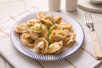 Plate of delicious boiled dumplings with green onion on white tile background, closeup