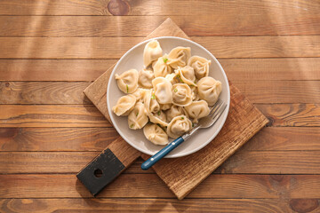 Plate with delicious boiled dumplings on wooden background