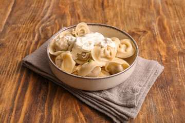 Bowl of delicious boiled dumplings with sour cream and green onion on wooden background, closeup