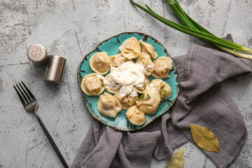Plate of delicious boiled dumplings with sour cream and green onion on grey background