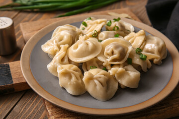 Plate of delicious boiled dumplings with green onion on wooden background, closeup
