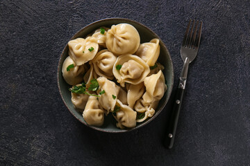 Bowl of delicious boiled dumplings with green onion and parsley on dark background