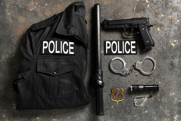 Handcuffs, police uniform and weapon on grey background
