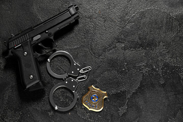 Handcuffs, gun and police shield on dark background