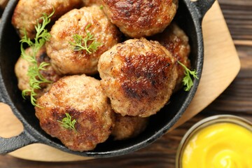Tasty patties, dill in frying pan and mustard on wooden table, flat lay