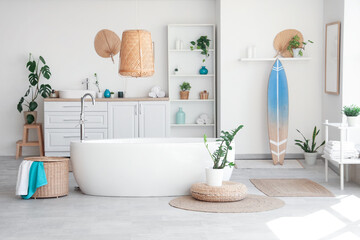 Interior of light bathroom with bathtub, houseplants and surfboard