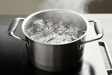 Cooking pot with boiling water and stove on table against grey background, closeup