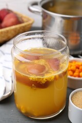 Tasty compot in glass jar and ingredients on grey wooden table, closeup