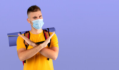 Travel ban during coronavirus pandemic concept. Serious millennial guy with camping gear wearing...