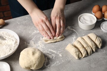 Woman kneading raw dough at light grey table, closeup
