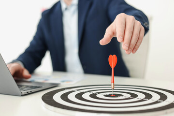 Man working on laptop at table, focus on dartboard with arrow indoors