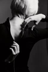 Stylish young woman with short blonde hair adjusting her black zip-up shirt, showcasing elegance and confidence with a neutral dark background.